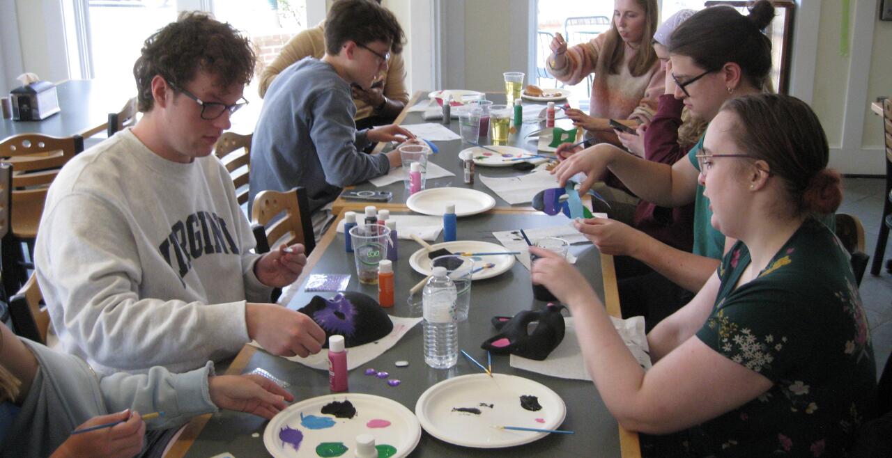 Students paint paper face masks with at a table
